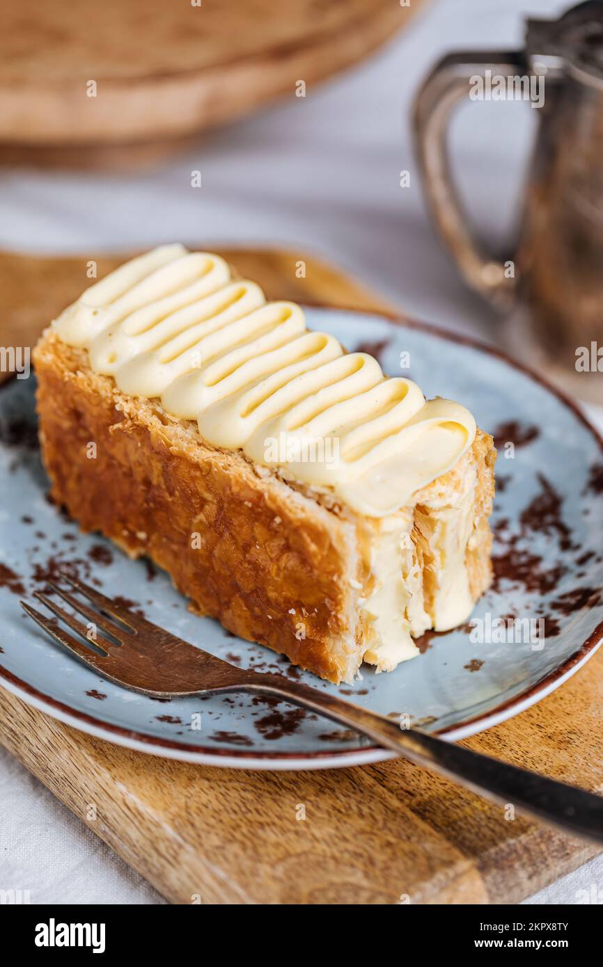 Französisches Dessert namens Mille Feuille oder Napoleon Kuchen auf rustikalem Holzbrett. Mehrlagiger leckerer Kuchen mit Vanillecreme und Blätterteig. Stockfoto