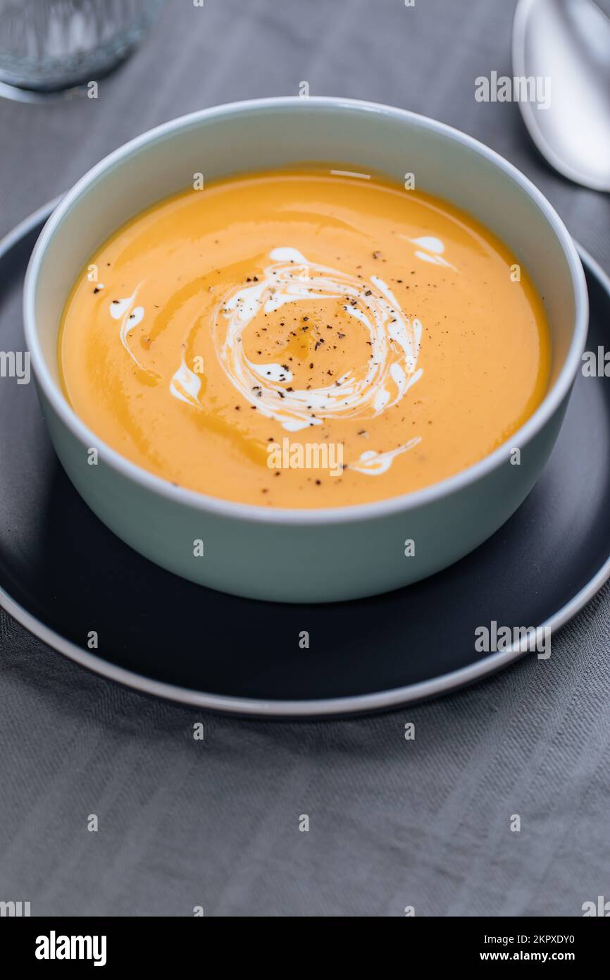 Cremige Kürbissuppe garniert mit Kochsauce, serviert in einer türkisfarbenen Schüssel auf dezentem grauem Hintergrund. Warme Speisen der Saison. Herbstvorspeise Stockfoto