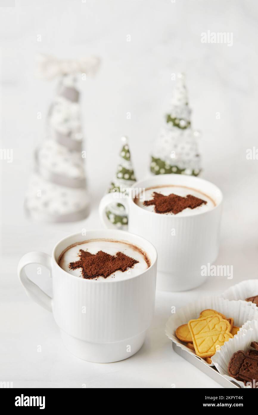 Nahaufnahme von zwei Tassen mit heißer Schokolade, Weihnachtskeksen und Weihnachtsdekorationen auf einem Tisch Stockfoto