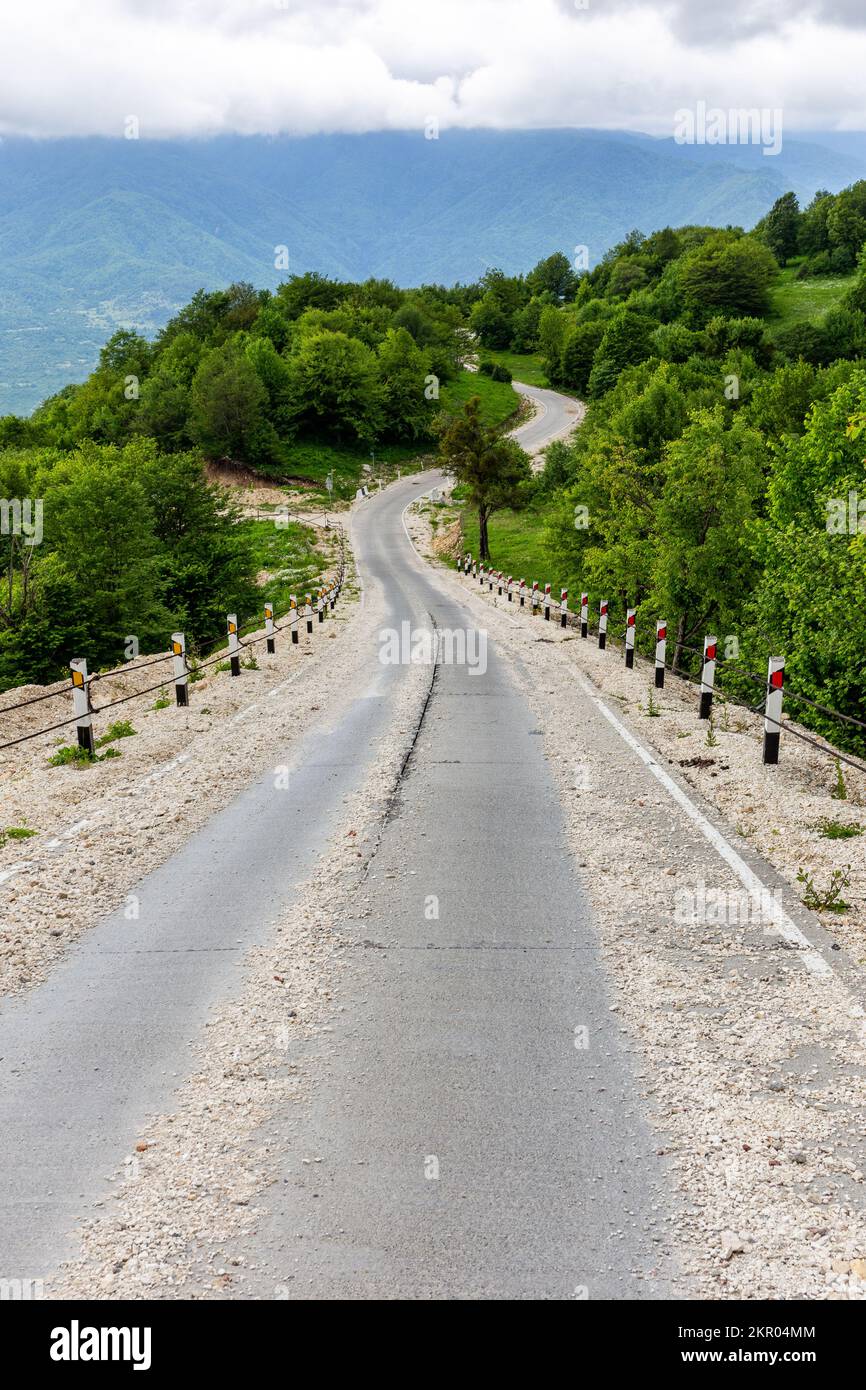 Ländlicher Asphalt verschlungene, mit losen Steinen und Kies bedeckte Straße vom Khvamli Berg hinunter zum Tskhenistsqali-Flusstal mit üppigem Grün Stockfoto