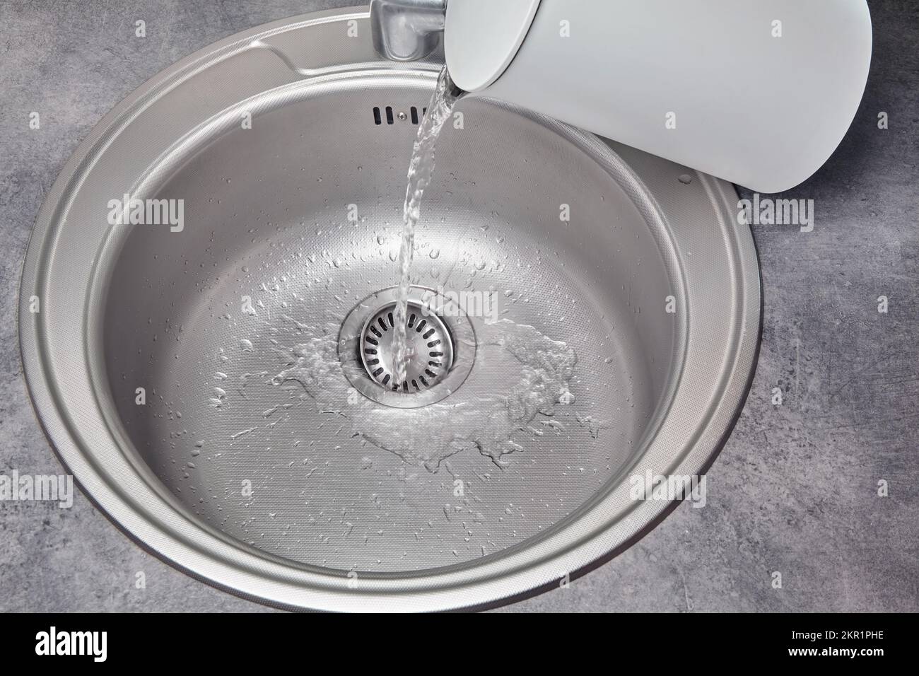 Heißes Wasser gießt aus einem weißen elektrischen Wasserkocher in ein Metallspüle. Schmutzreinigung und -Desinfektion Stockfoto