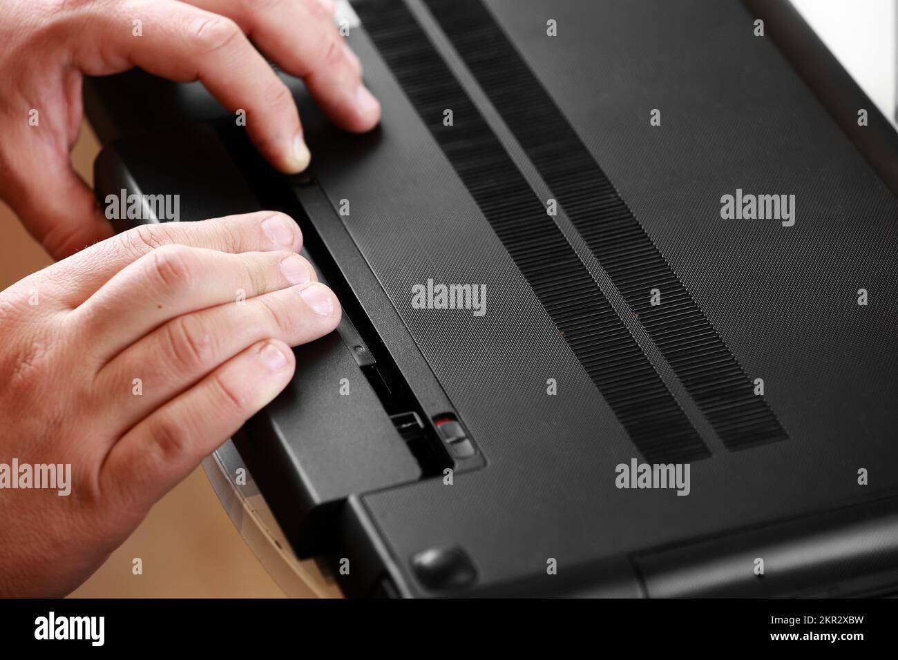 Die Hände des Reparaturmanns, der den Akku aus dem Laptop entfernt ...