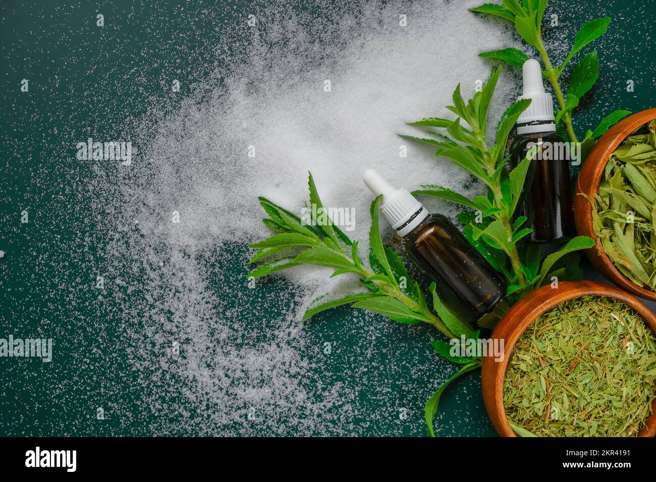 Süße Pflanze. Stevia rebaudiana. Trockener Stevia, Pulver und flüssiger Stevia-Extrakt in einer Glasflasche auf dunkelgrünem Hintergrund. Natürlicher Zuckerersatz Stockfoto