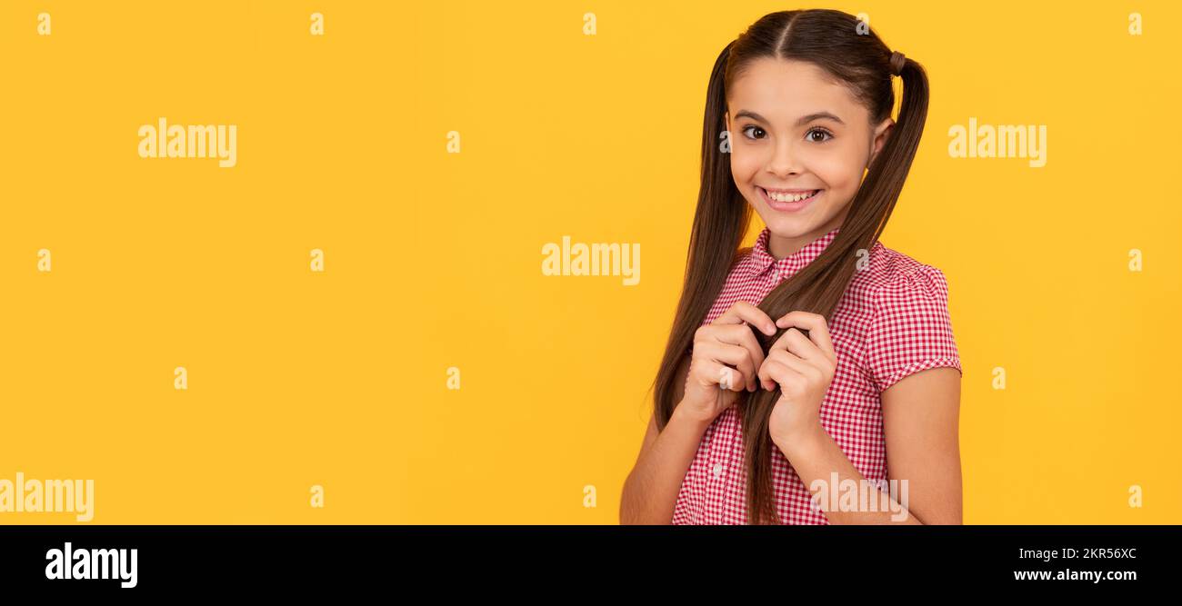Hübsches Mädchen mit schüchterem Lächeln, das Haar mit gelbem Hintergrund berühren. Kindergesicht, horizontales Poster, isoliertes Porträt eines Teenagers, Banner mit Kopie Stockfoto