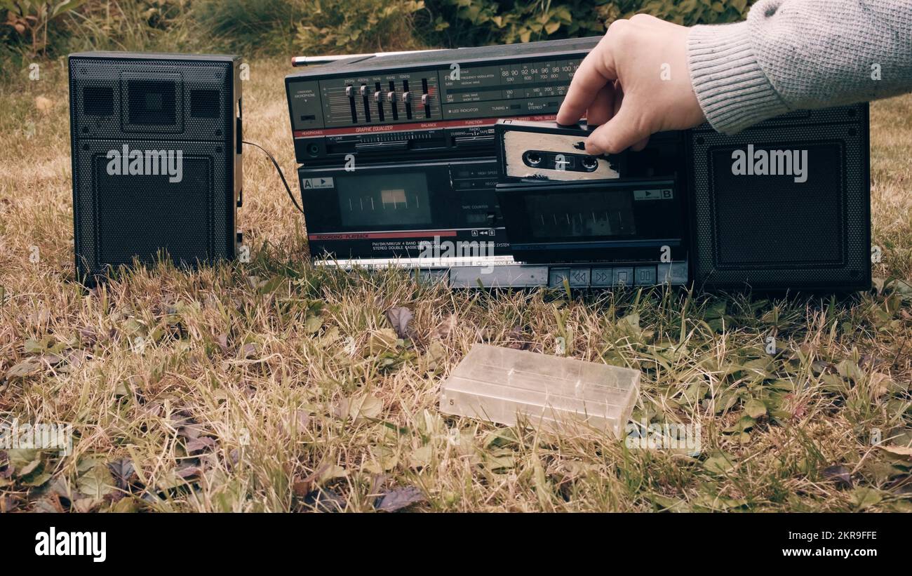 Der Mann nimmt die Kassette aus dem Koffer und legt sie in den alten Retro-Rekorder ein Stockfoto