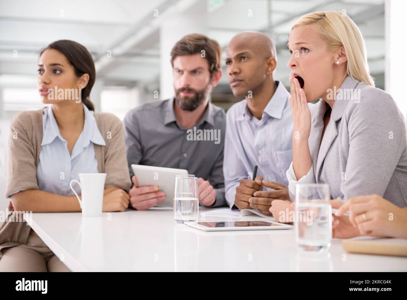 Zeit, ein paar neue Ideen zu hören. Eine Geschäftsfrau, die während eines Meetings mit ihren Kollegen gähnt. Stockfoto