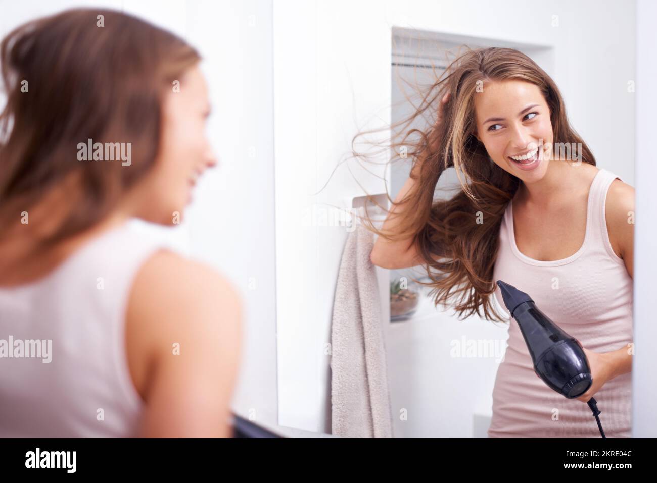 Kümmert sich um ihre üppige Mähne. Eine junge Frau föhnt ihr Haar vor einen Spiegel. Stockfoto