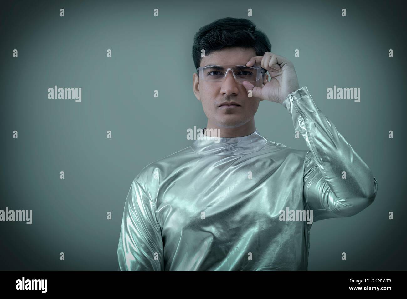 Ein Mann, der silberne, futuristische Kleidung trägt, eine Brille hält und in die Kamera schaut, Zukunftstechnologie-Konzept Stockfoto