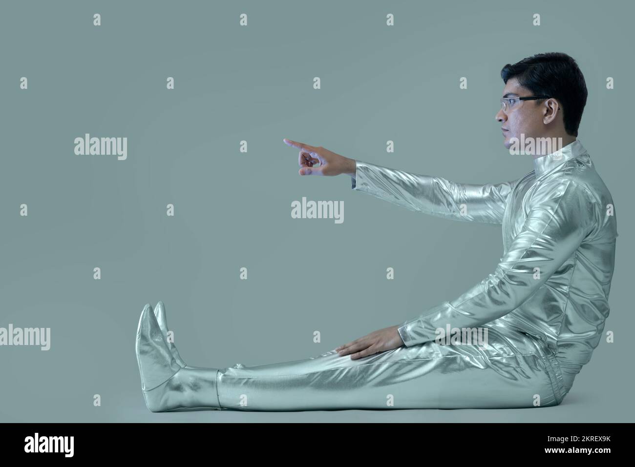 Seitenansicht eines Mannes in silbernem Kleid, der mit dem rechten Arm sitzt und auf einen grauen Hintergrund zeigt, zukunftsweisendes Technologiekonzept. Stockfoto
