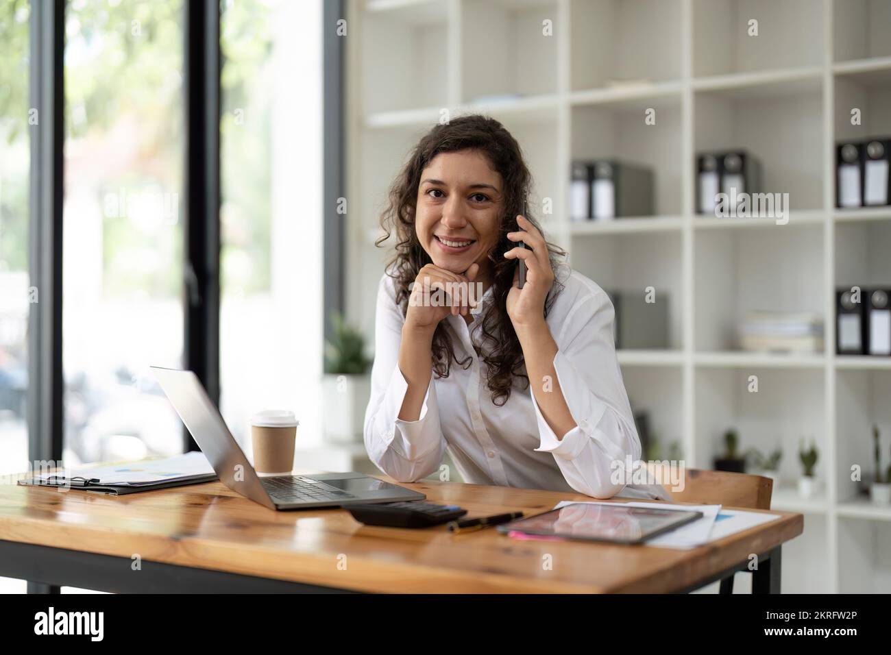 Porträtfrau, die aus der Ferne arbeitet, in die Kamera schaut, mit dem Smartphone spricht. Stockfoto