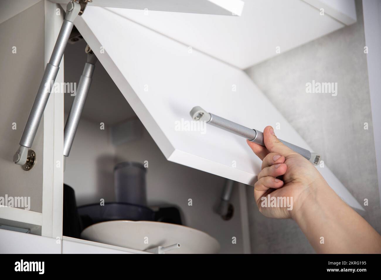 Ein Möbelmontagearbeiter hält eine einhole Gasfeder, um eine Schranktür zu  öffnen und zu stützen. Moderne Möbel Stockfotografie - Alamy