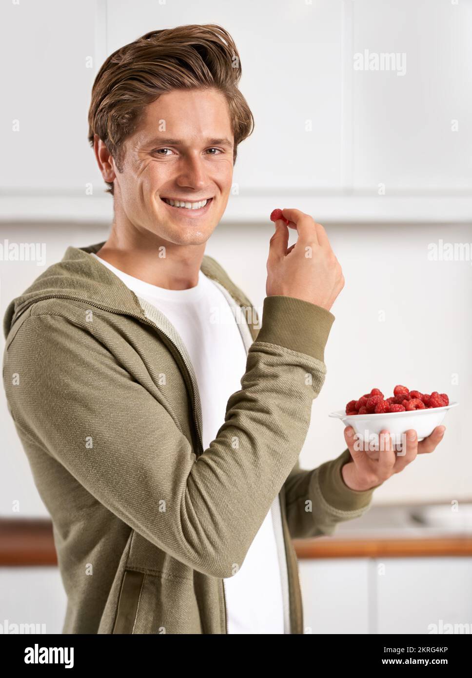 Beeren, die vor saftiger Güte platzen. Ein gutaussehender junger Mann, der eine Schüssel Himbeeren zum Frühstück isst. Stockfoto