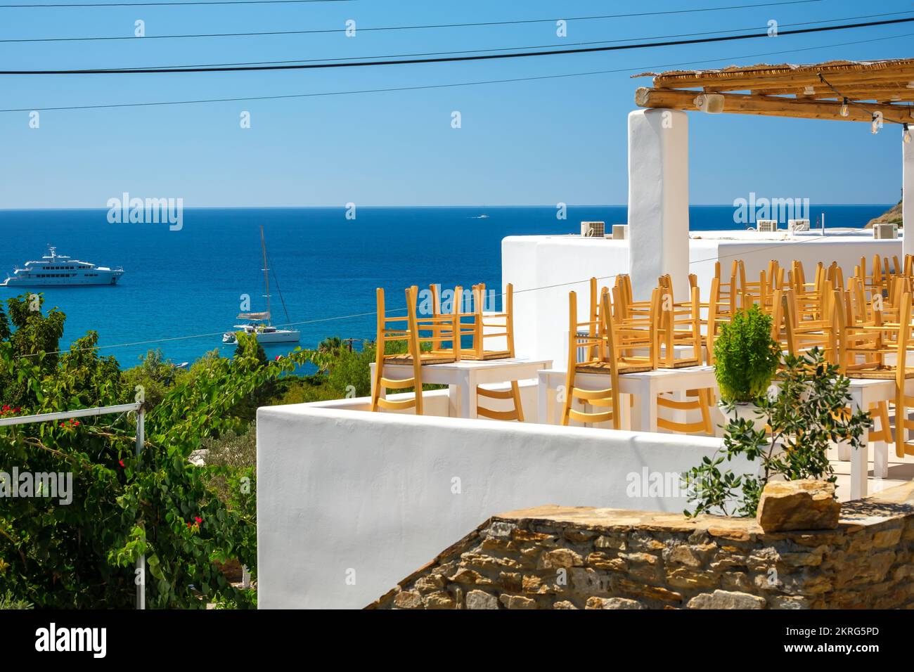 IOS, Griechenland - 15. September 2022 : Blick auf eine geschlossene Restaurantterrasse mit Stühlen, Tischen und den Mylopotas-Strand im Hintergrund in iOS Greece Stockfoto