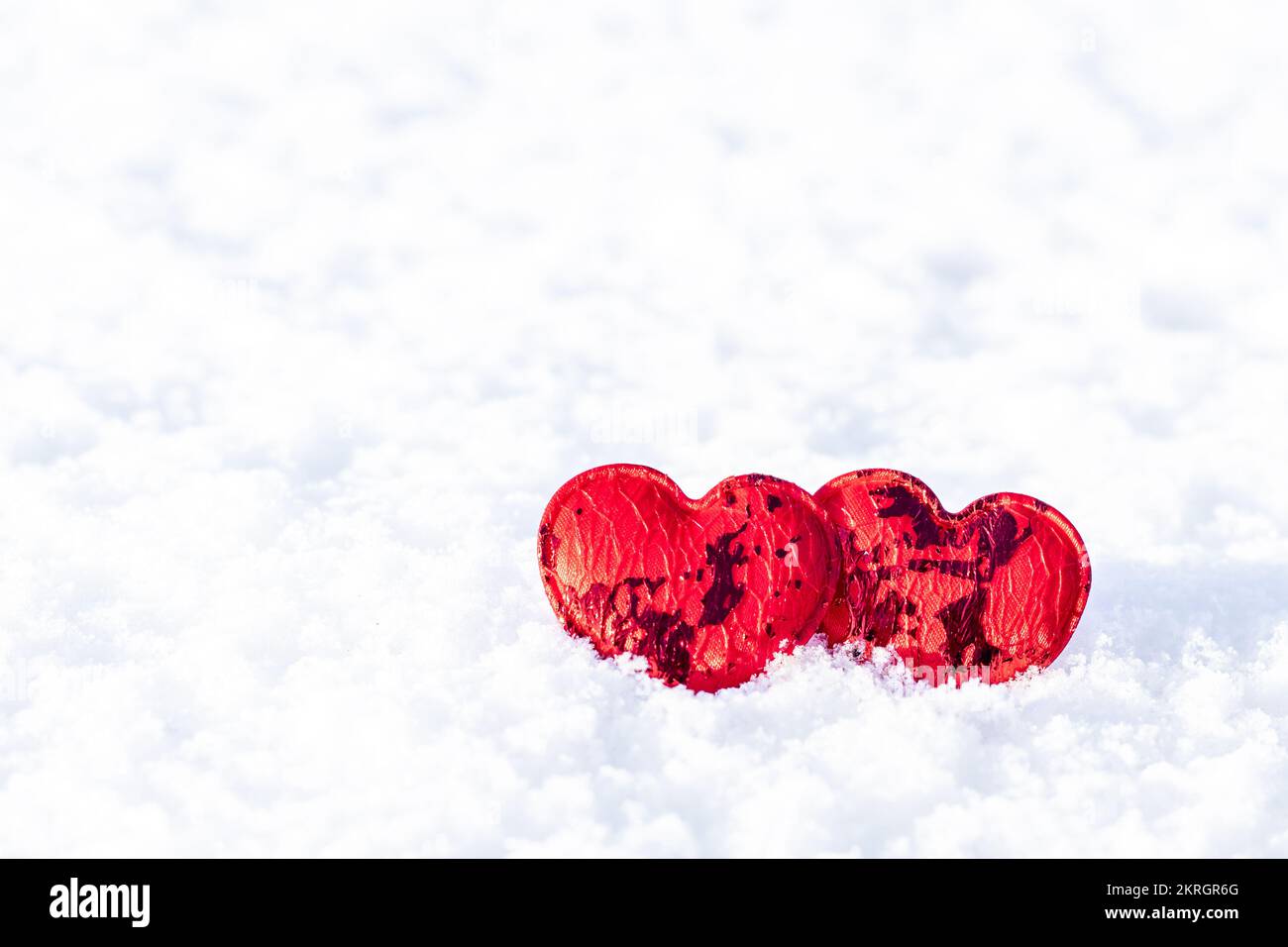 Zwei rote Herzen auf einem Hintergrund von weißer Schneefallaufnahme. Valentinstag-Konzept. Valentinstag. Platz für eine Inschrift. Kopierraum. Stockfoto