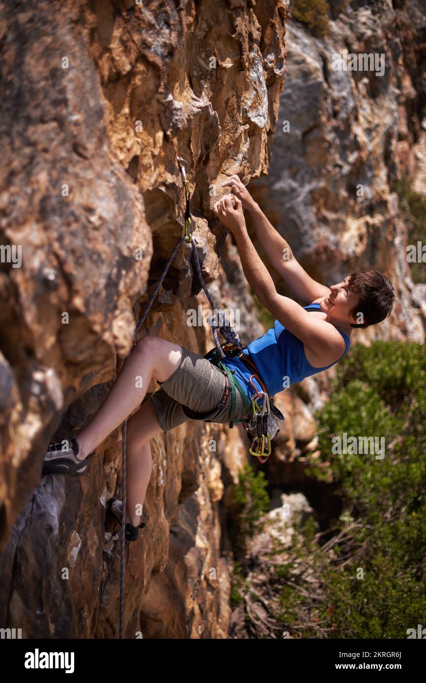 Dadurch fühlt sie sich lebendig. Eine junge Frau, die beim Klettern einen Felsvorsprung greift. Stockfoto