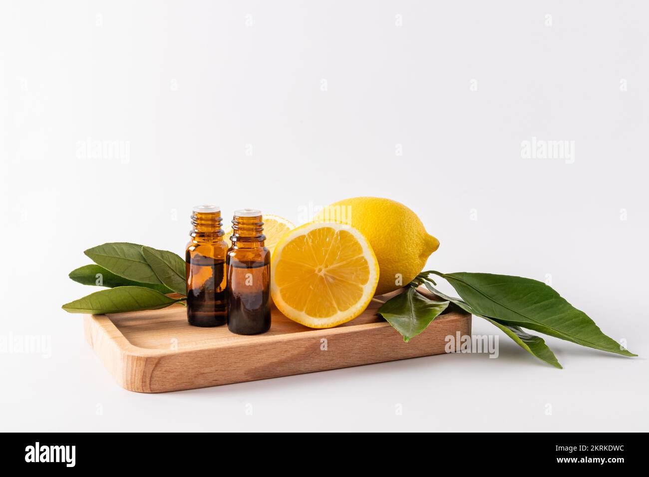Zwei medizinische Flaschen mit einem Tropfer mit ätherischem Zitronenöl stehen auf einer Holzschale inmitten reifer Zitronen. Aromatherapie. Massage. Antioxidans. Vitamin C Stockfoto