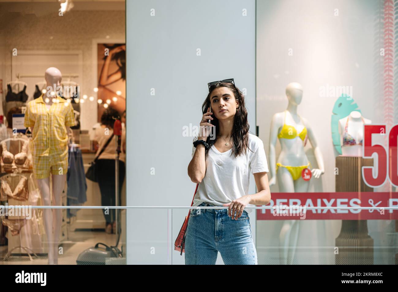 Junge Frau, die zuhört und telefoniert, in der Nähe einer Boutique mit Rabatten und Sommerbekleidung Stockfoto