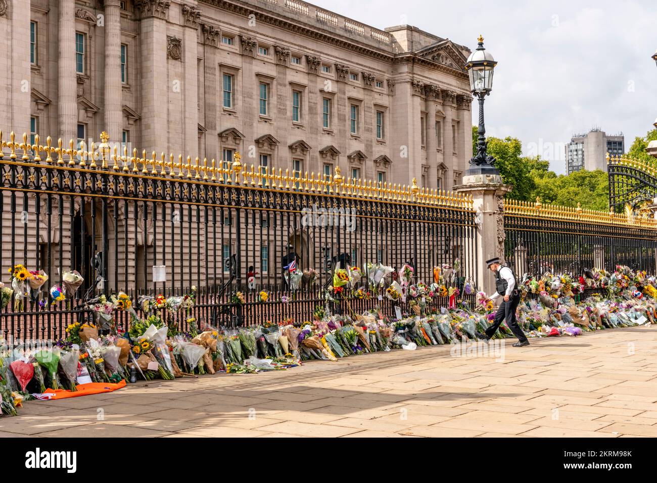 Ein Polizist platziert Blumen, die Ihm Von Einem Mitglied der Öffentlichkeit gegeben wurden, vor den Toren des Buckingham Palace nach dem Tod der Königin, London, Großbritannien. Stockfoto