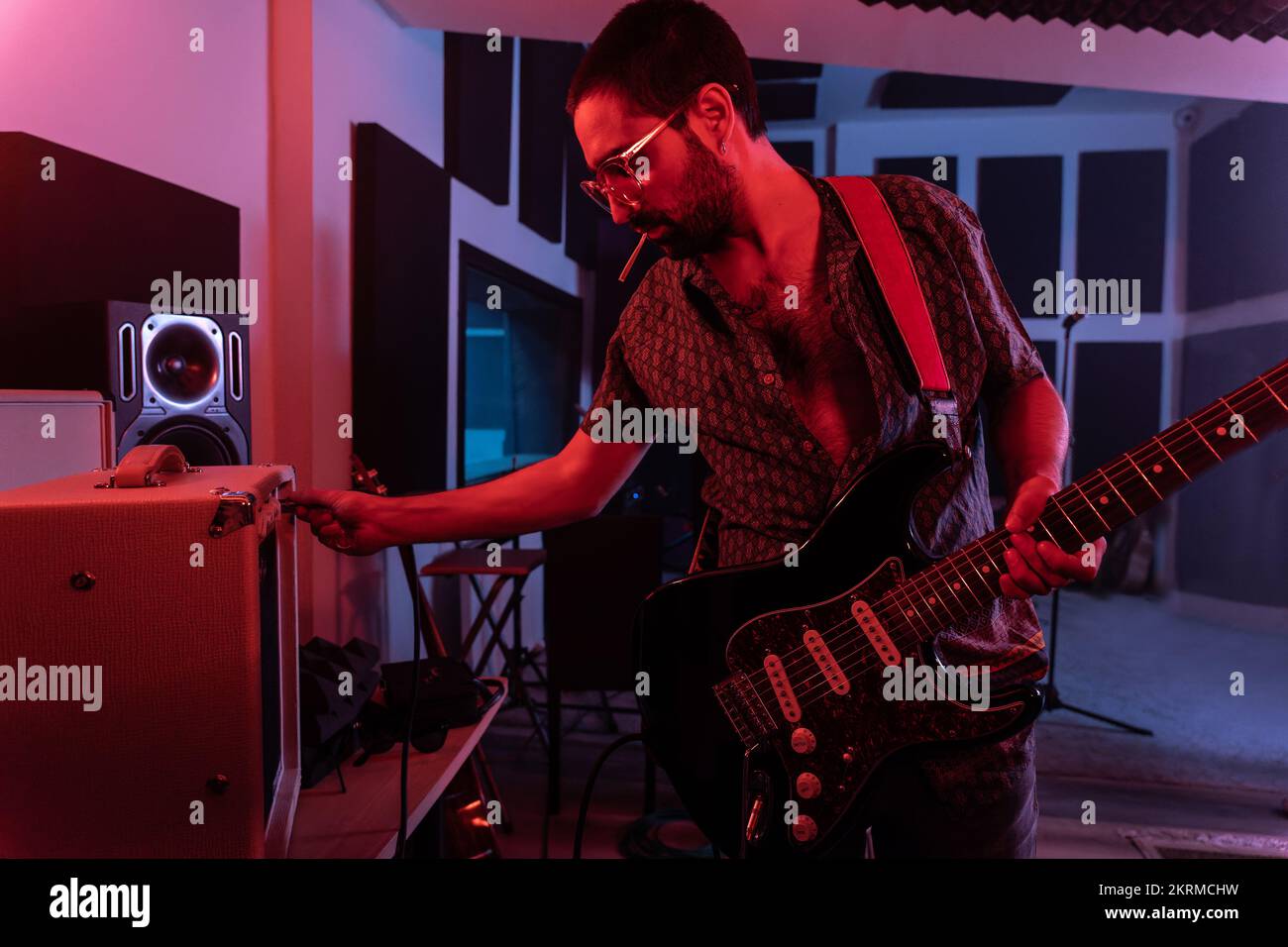 Männlicher Musiker in Freizeitkleidung mit elektrischem Gitarrenverstärker im modernen beleuchteten Studio Stockfoto