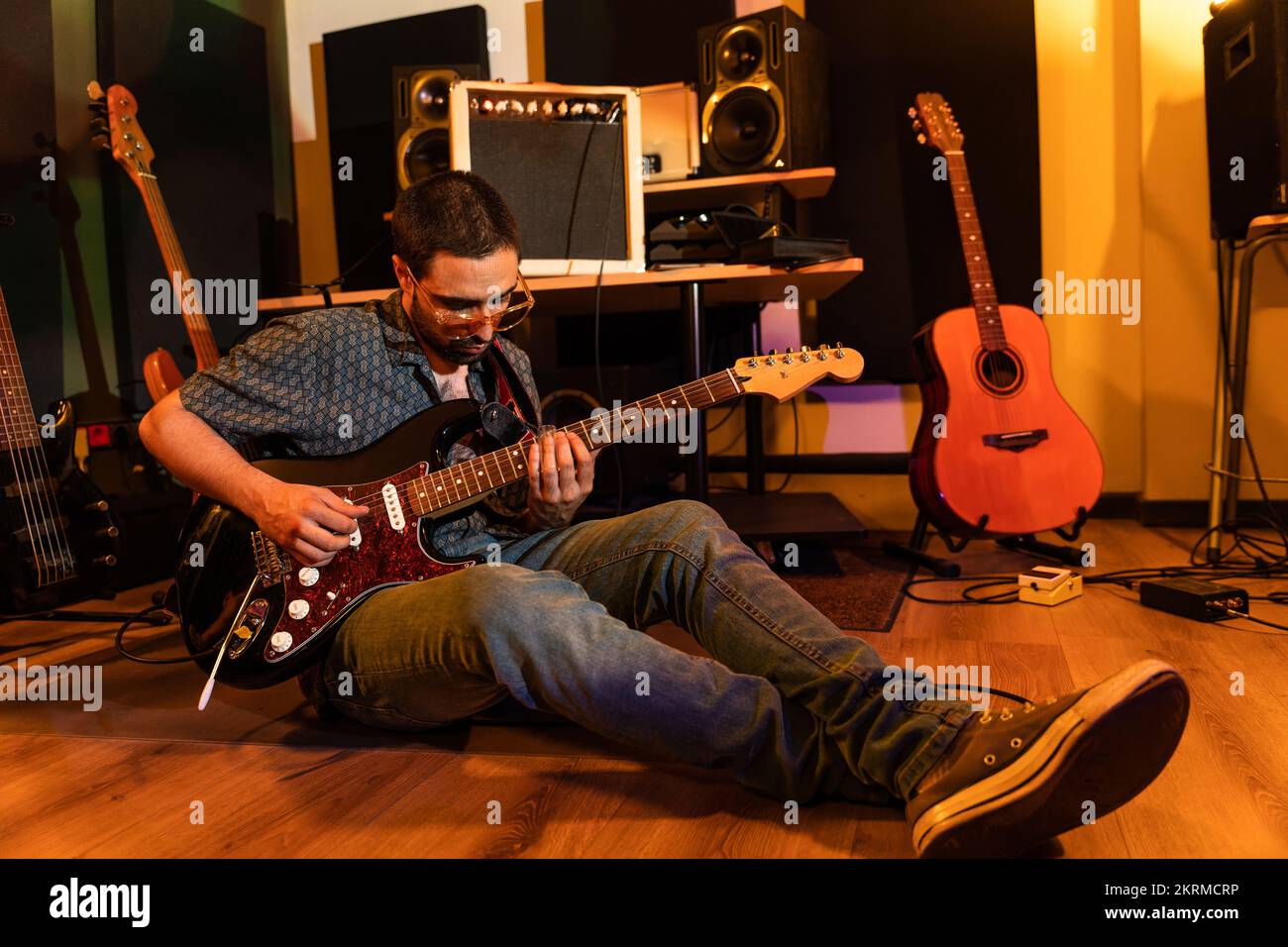 Ein ganzer männlicher Musiker in Freizeitkleidung, der auf dem Boden sitzt und im Studio Musik spielt Stockfoto