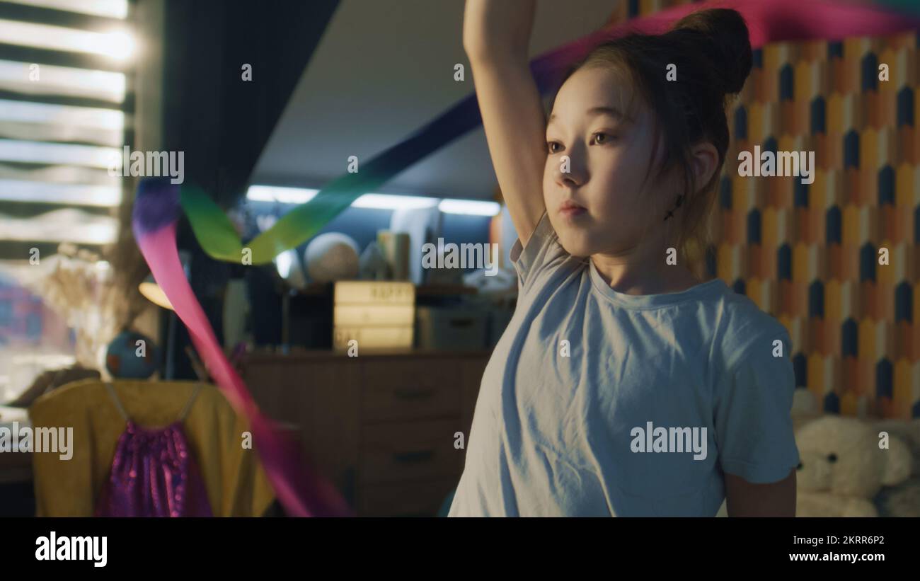Das junge asiatische Schulmädchen dreht sich um sich herum und trainiert neue visuelle Bewegungen. Rhythmische Gymnastik. Sport-Hobby. Physische Integrität wird in Quarantäne aktualisiert. Zeitlupe. Hochformat. Stockfoto