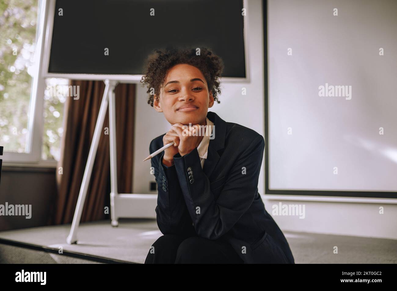 Frau mit Bleistift, die in die Kamera schaut, sitzt im Büro Stockfoto