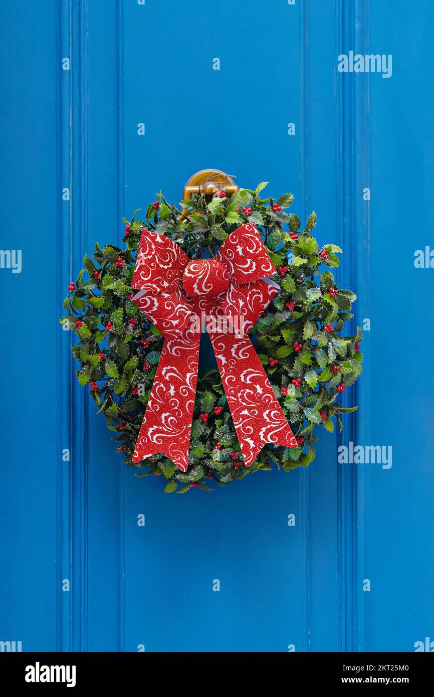 Traditioneller grüner und roter Weihnachtskranz hängt an der blauen Eingangstür des Hauses. Traditionelle Einrichtung zu Weihnachten Stockfoto