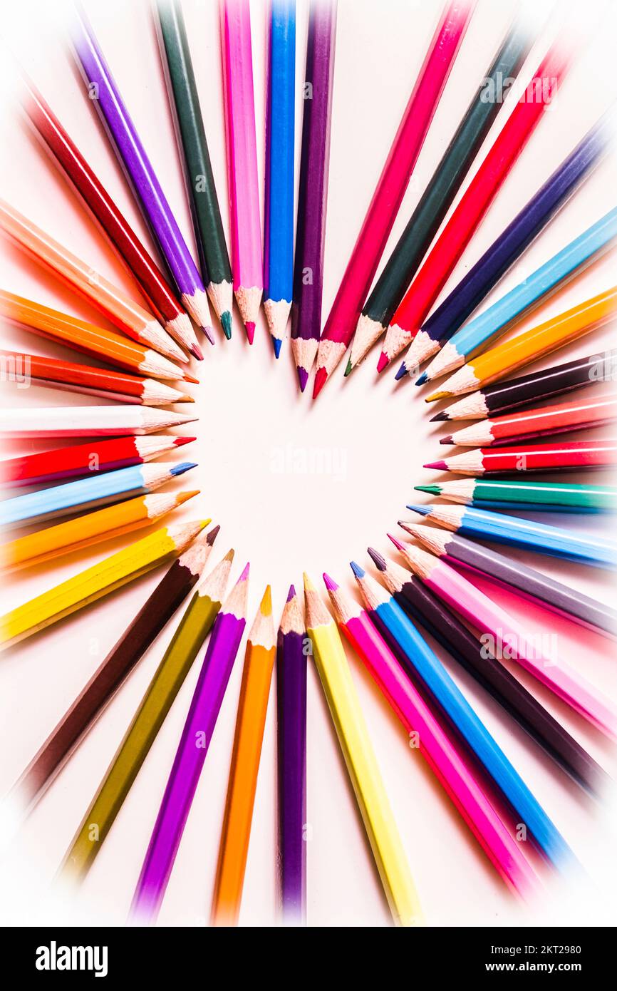 Anordnung der farbigen Bleistiftzeichnen, die in einer herzförmigen Mitte mit leerem Kopierraum in einem Romantik- oder Liebesthema zusammenlaufen, Ansicht von oben auf weißem Witz Stockfoto