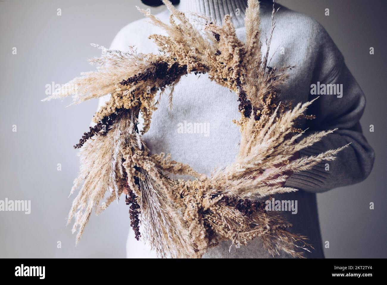 Stilvoller Herbstkranz. Hände mit trockenem Gras, Wildblumen und Weizenkranz Stockfoto
