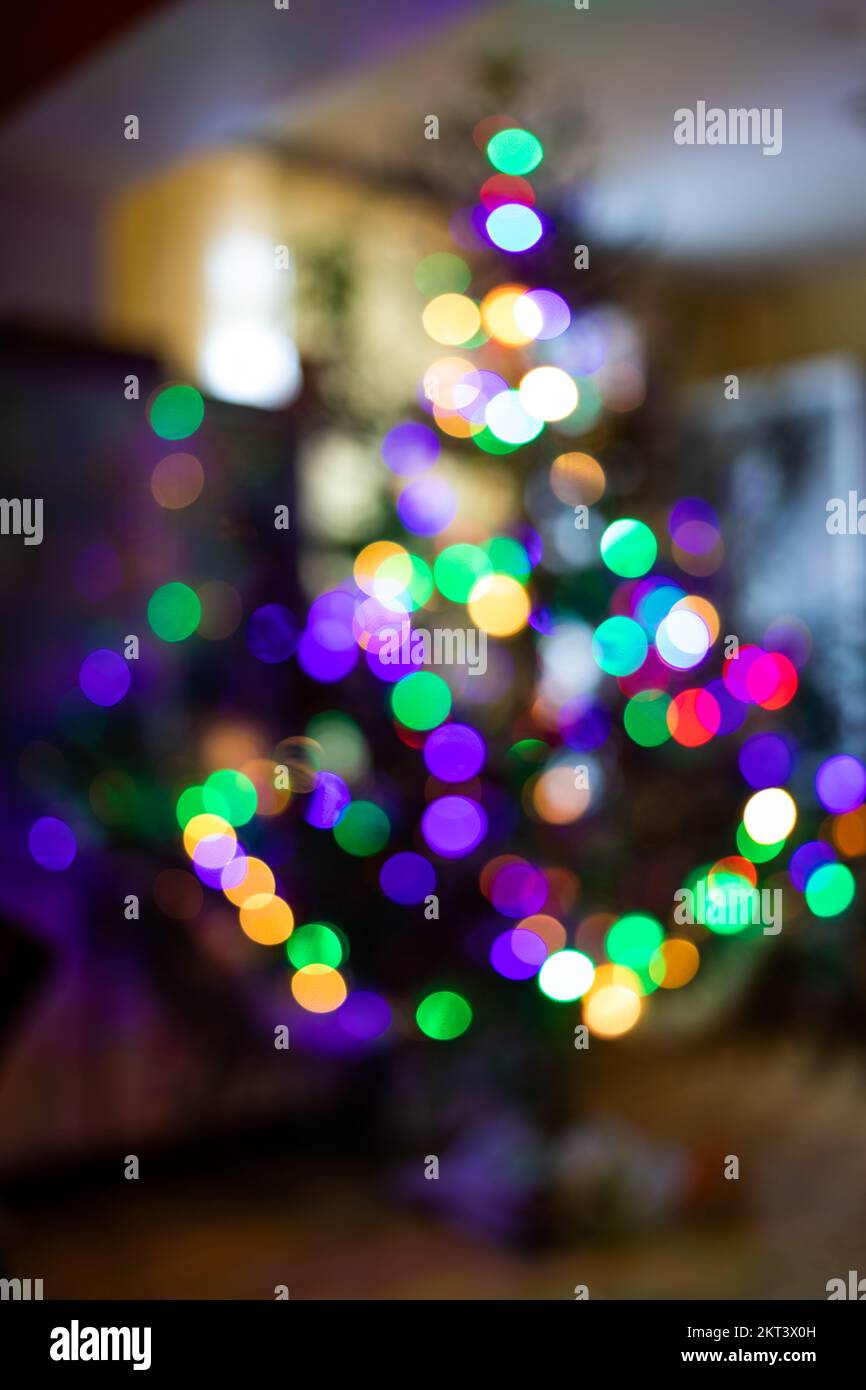 Silhouette eines glitzernden traditionellen Weihnachtsbaums im Innenraum. Verschwommenes, helles Licht von Girlanden in Form eines Weihnachtsbaums. Weihnachtsbaum mit bunten Farben Stockfoto