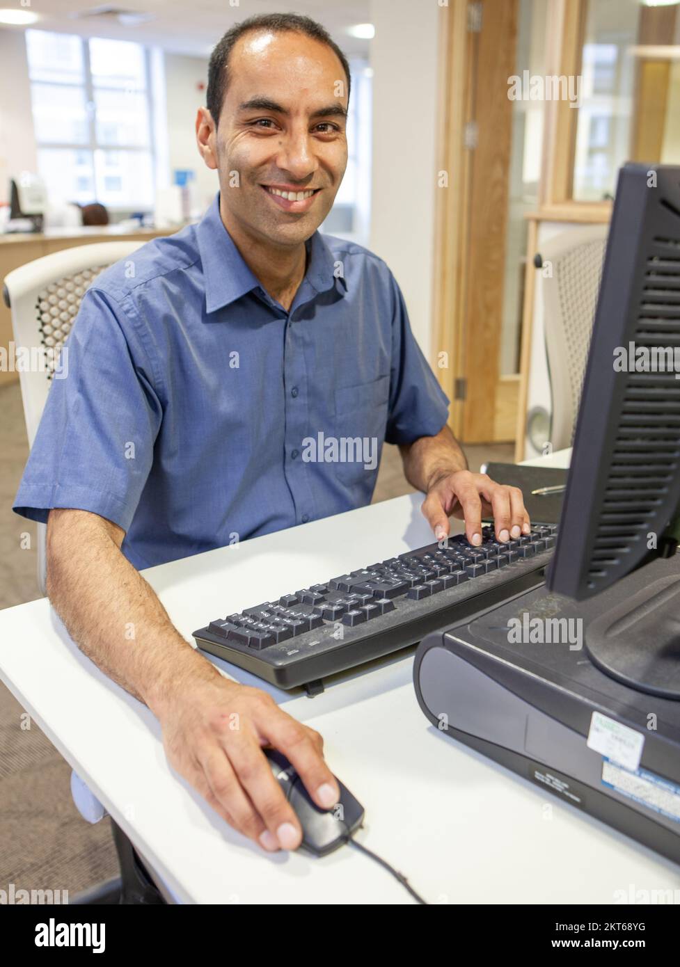 Computer Studies, Lehrer an seinem Schreibtisch. Ein reifer südasiatischer Mann in einer Bildungseinrichtung, der an seinem Computer sitzt. Aus einer Reihe von zugehörigen Bildern. Stockfoto