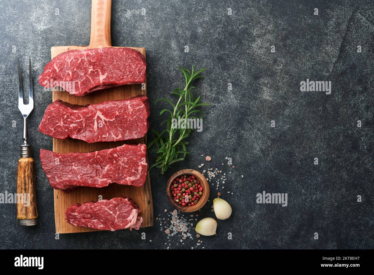 Rohe Steaks. Top Blade Steaks auf Holzbrettern mit Gewürzen, Rosmarin, Gemüse und Zutaten zum Kochen auf schwarzem Hintergrund. Draufsicht. Kopieren en Stockfoto