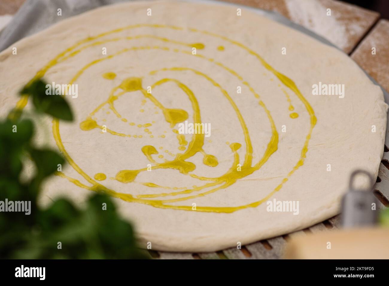 Geben Sie extra natives Olivenöl auf den Teig für Pizza auf einem Holzbrett mit Zutaten und Werkzeugen, Nahaufnahme Stockfoto