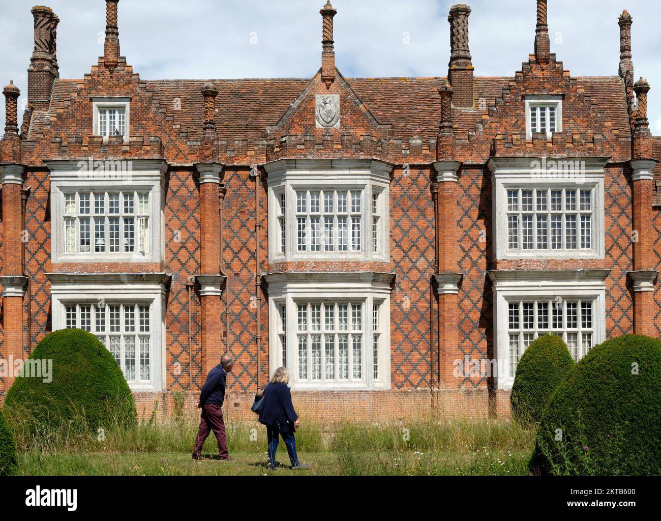 Besucher, die an der Erhebung der wunderschönen, verzierten roten Ziegelsteine der Helmingham Hall and Gardens Suffolk vorbeispazieren Stockfoto