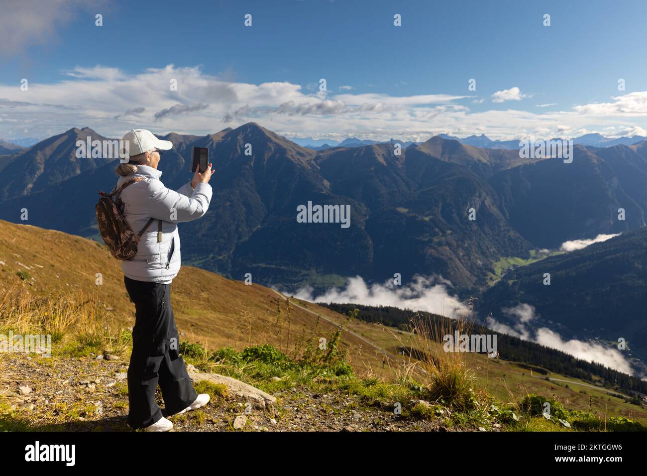 Eine Erwachsene Frau in Sportjacke, Hose und Mütze fotografiert eine Landschaft in den österreichischen Alpen. Hochwertiges Foto Stockfoto