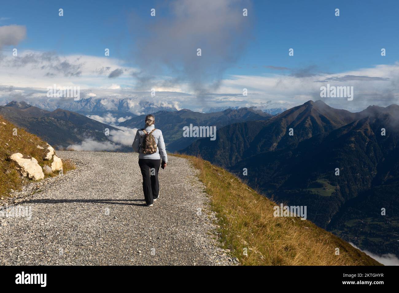 Eine grauhaarige Frau in Sportbekleidung geht in den alpen auf Wolkenhöhe entlang einer alpinen Straße. Hochwertiges Foto Stockfoto