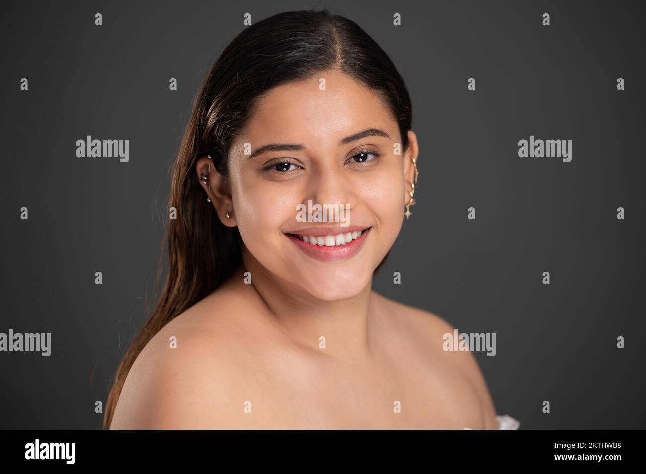 Porträtfoto eines lächelnden, hübschen Latino-Mädchens mit grauem Studiohintergrund Stockfoto