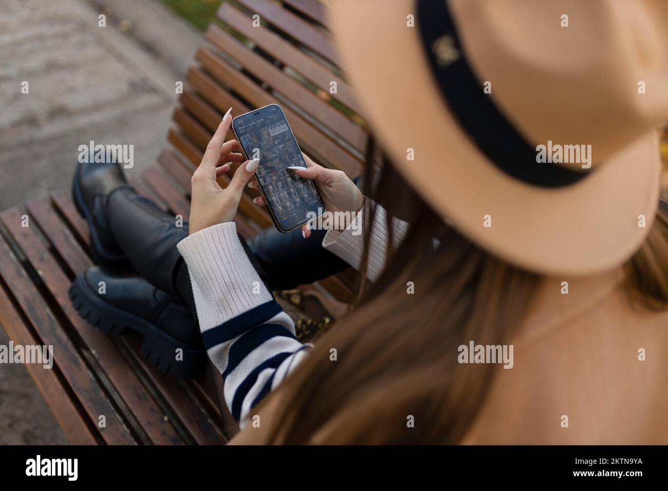 Attraktives, fröhliches braunes Mädchen im Trenchcoat mit Kaffee, das mit dem Mobiltelefon im Freien glücklich unterwegs ist Stockfoto