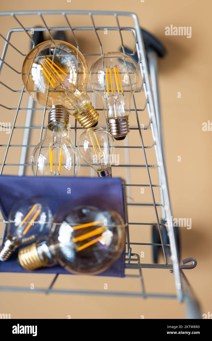 Viele elektrische Lampen in einem Einkaufswagen.Verbrauch und Bezahlung für Energieverbrauch.Glühbirnen in einem Wagen auf beigem Hintergrund.Krise im Stockfoto