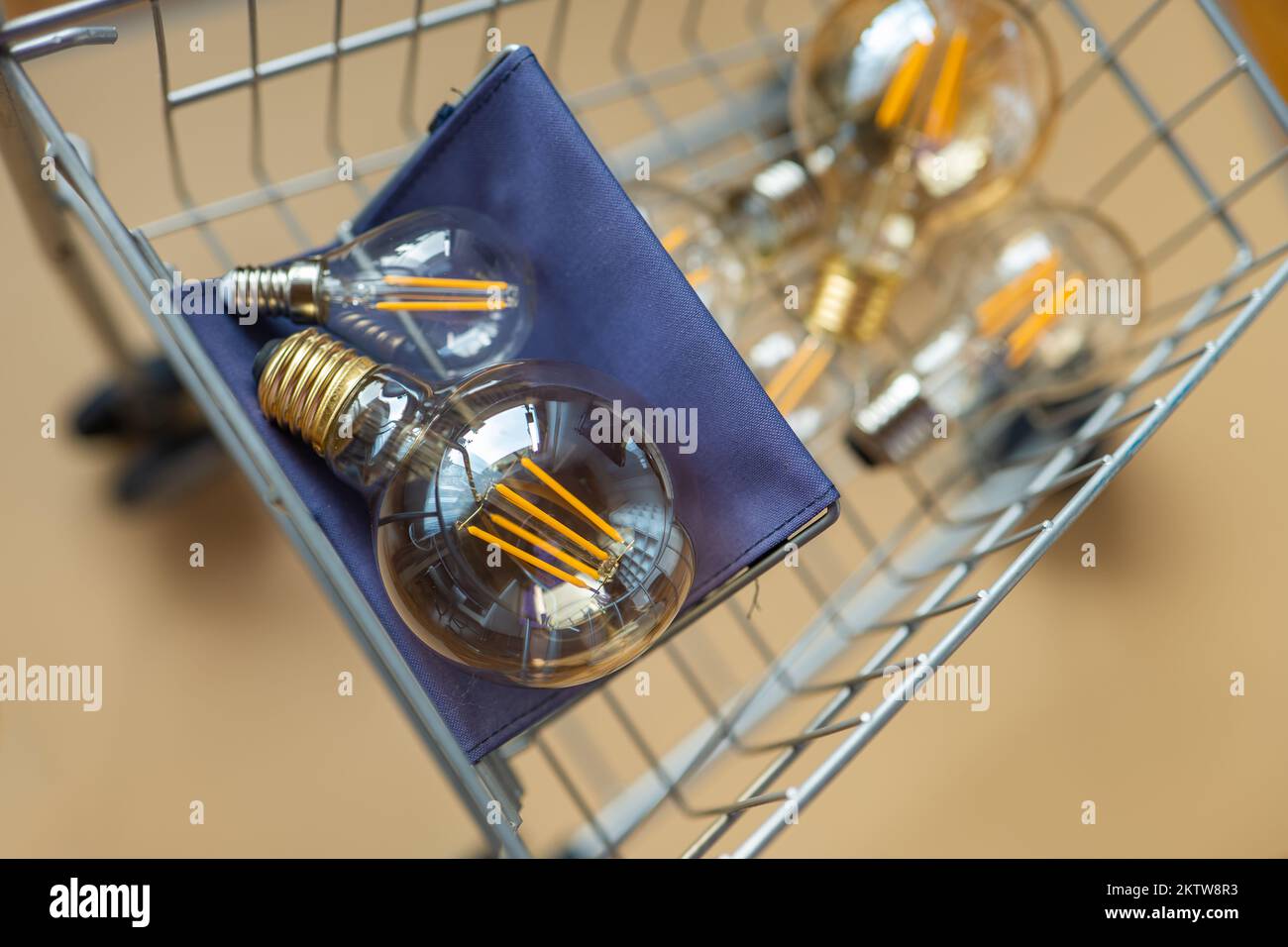 Verbrauch und Bezahlung des Energieverbrauchs. Kauf von Elektrizität. Viele elektrische Lampen in einem Einkaufswagen. Glühbirnen in einem Wagen in Beige Stockfoto