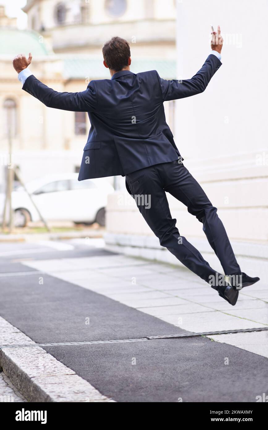 Auf der Spitze der Geschäftswelt. Rückansicht eines Geschäftsmanns, der vor Freude auf einem Bürgersteig sprang. Stockfoto