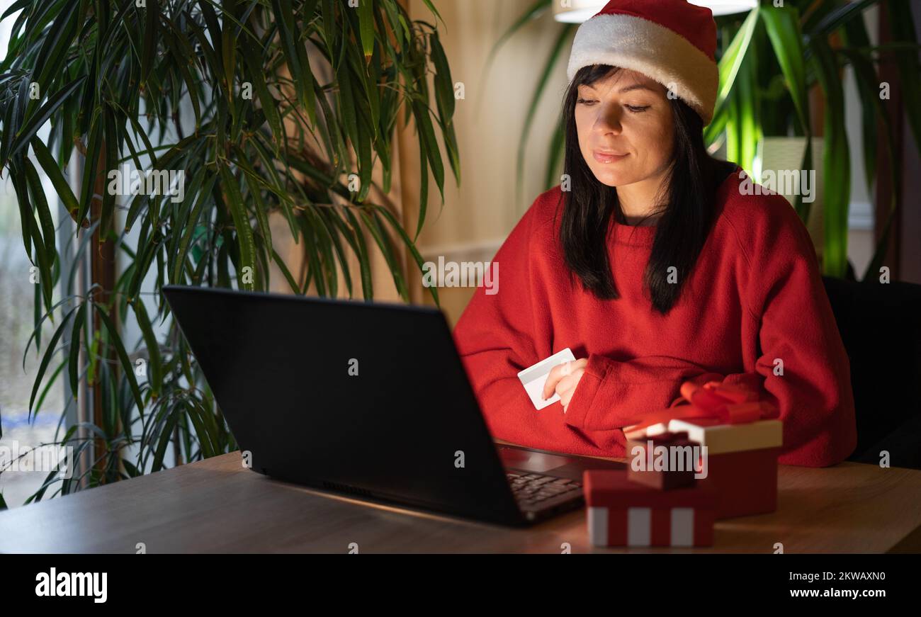 Eine besorgte Frau in Santa hat, die einen Laptop und eine Kreditkarte benutzt, ist über Geldmangel, vergessenes Passwort und Probleme beim Kauf über das Internet verwundert Stockfoto