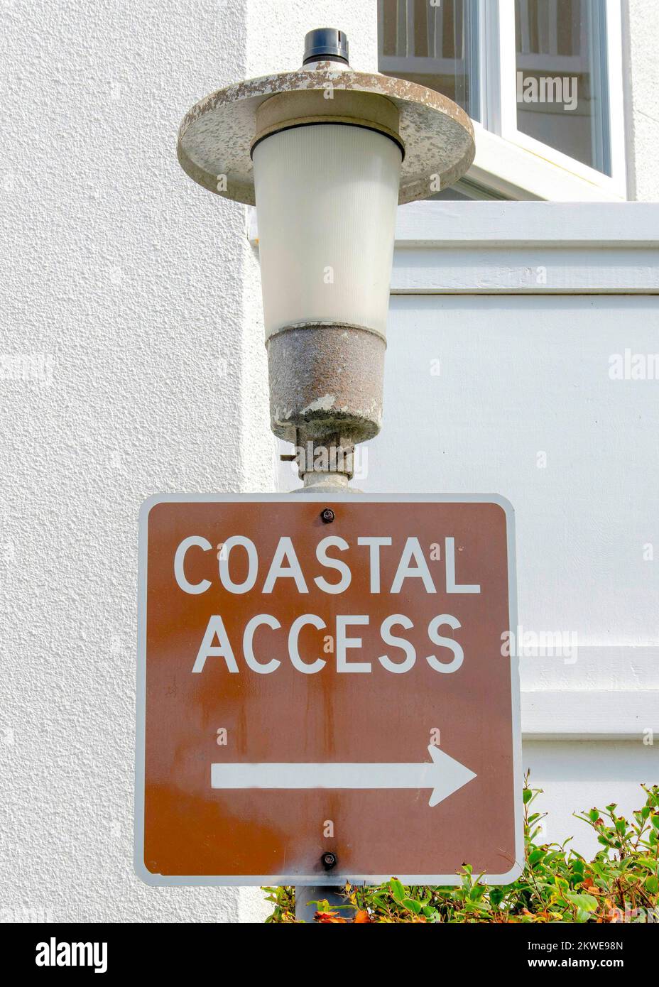 Vertikales Schild für den Küstenzugang an einer Laterne in La Jolla, Kalifornien. Nahaufnahme einer Beschilderung vor dem weißen Gebäude mit Geländern und Sträuchern draußen. Stockfoto