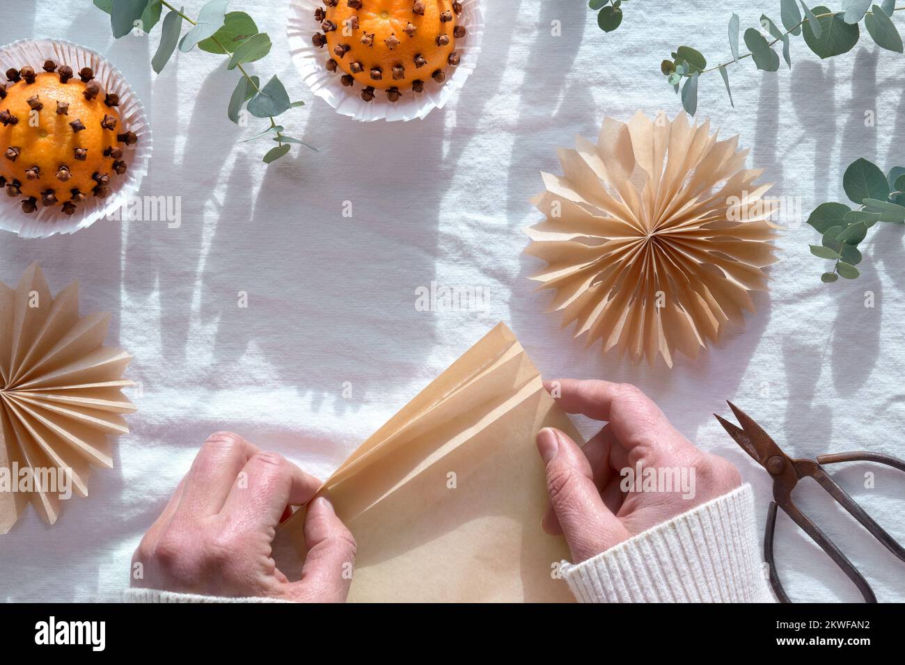 Duftende Pomander-Kugeln, handgefertigt aus Mandarinen und Nelken. Flach liegend auf weißem Textiltisch mit aromatisch wintergrünen Eukalyptuszweigen Stockfoto