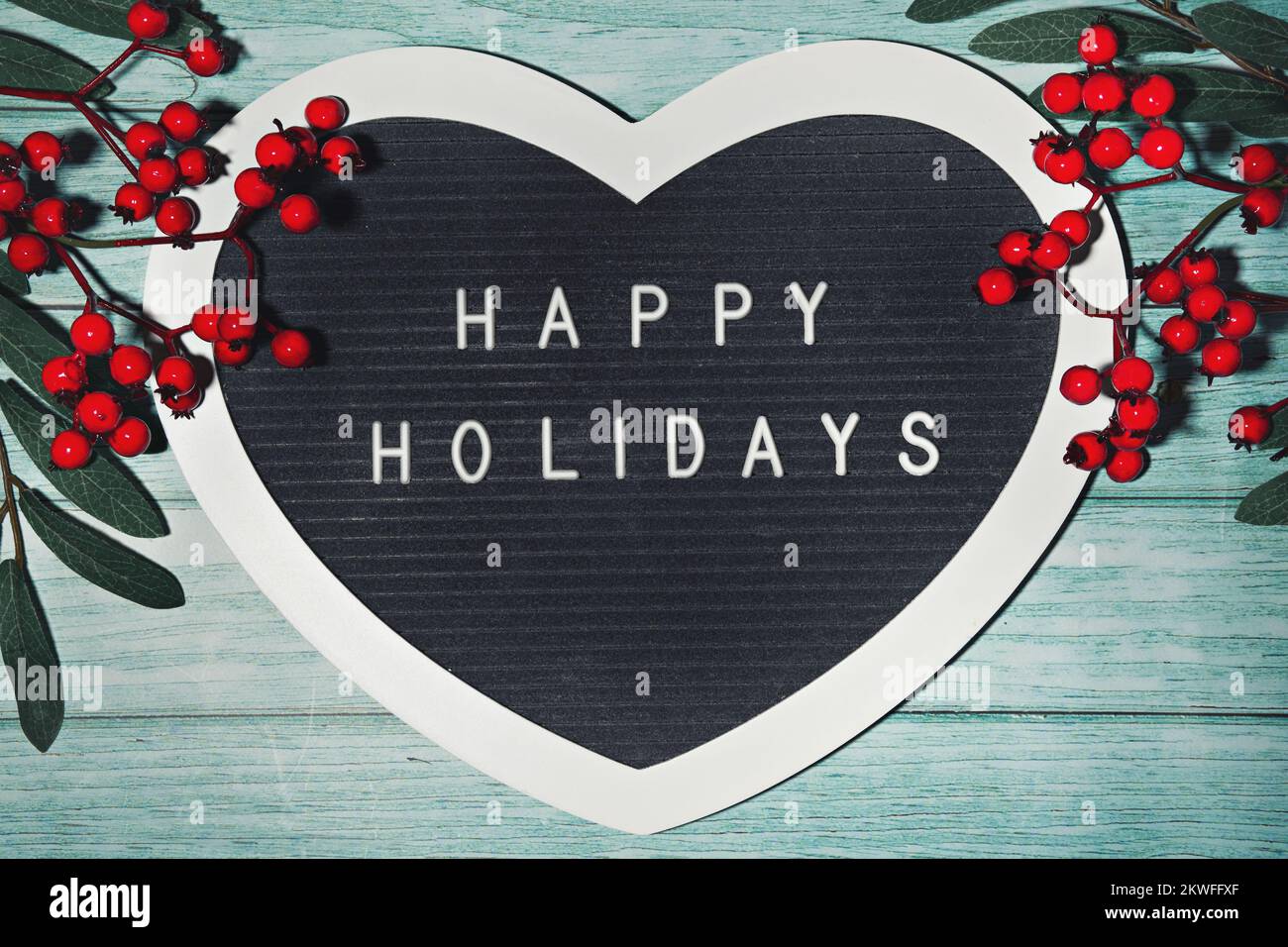 Schreiben Sie Happy Holidays auf herzförmigen Brieftafeln, Brieftafeln. Winterweihnachtsdecke mit Rowan-Beere auf mintgrünem Holz mit Schnee Stockfoto