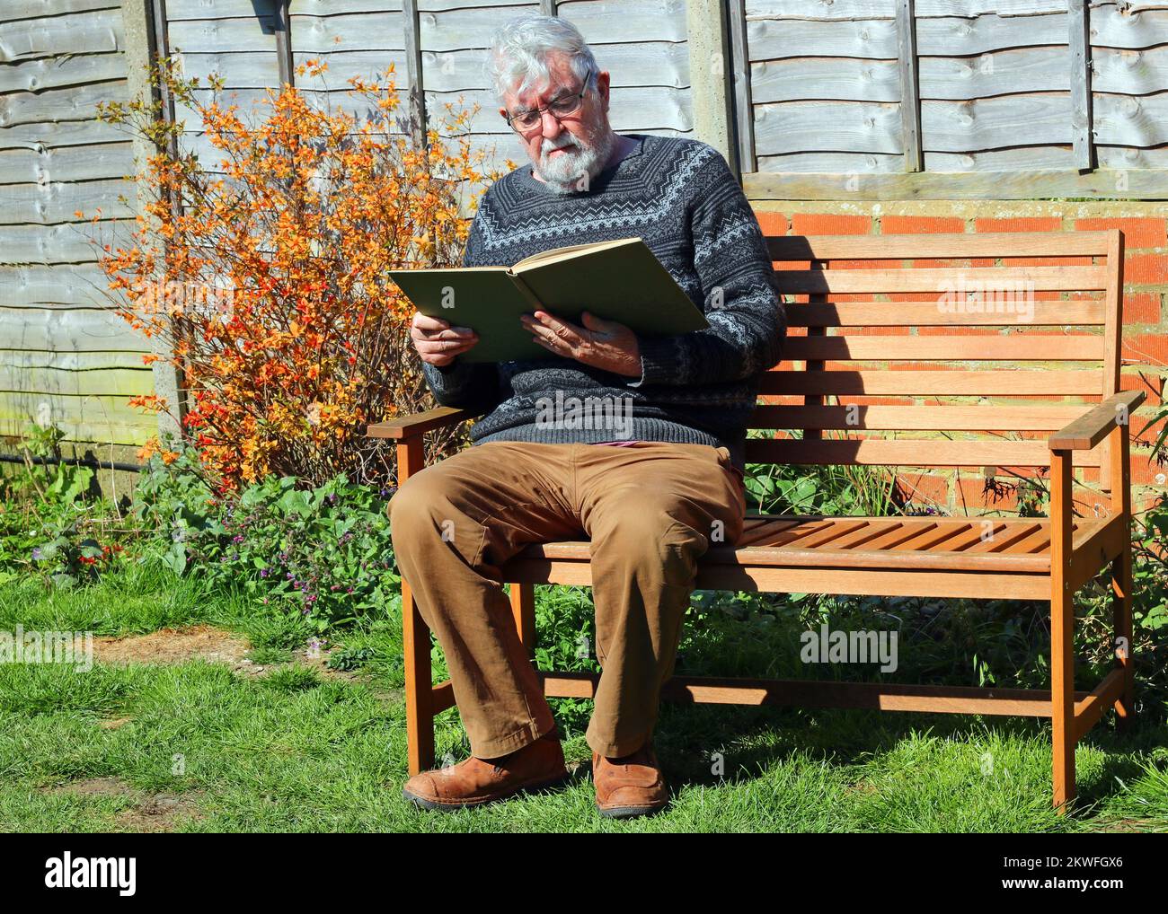 Älterer oder älterer Mann, der draußen in der Sonne sitzt und ein Buch liest. Stockfoto