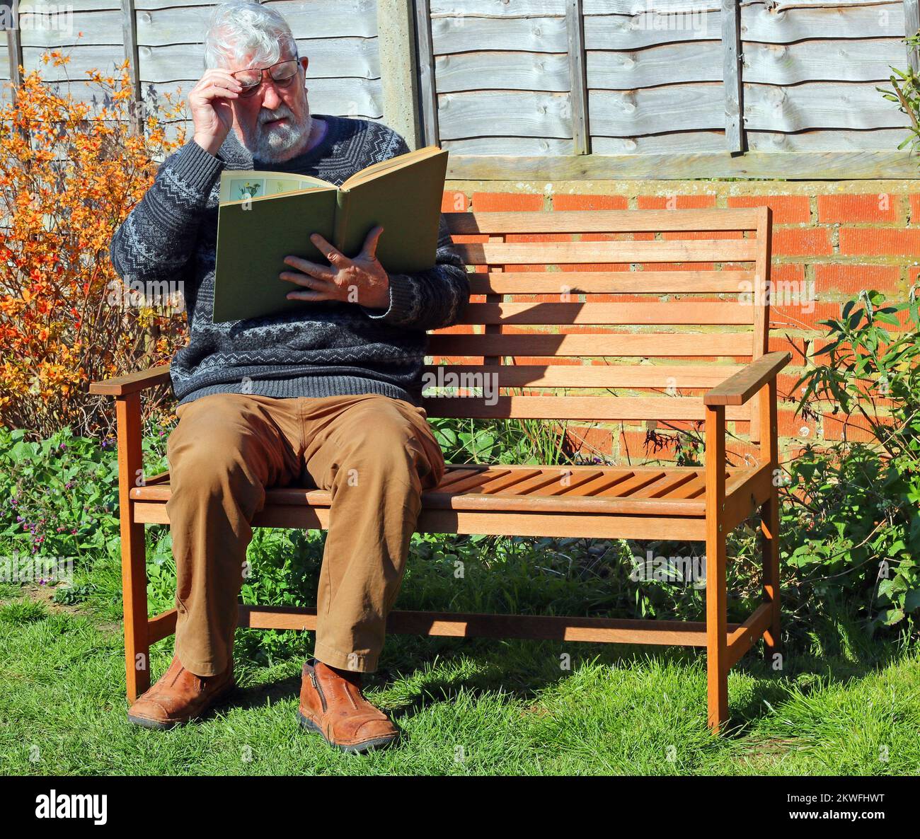 Älterer oder älterer Mann, der draußen in der Sonne sitzt und ein Buch liest. Stockfoto