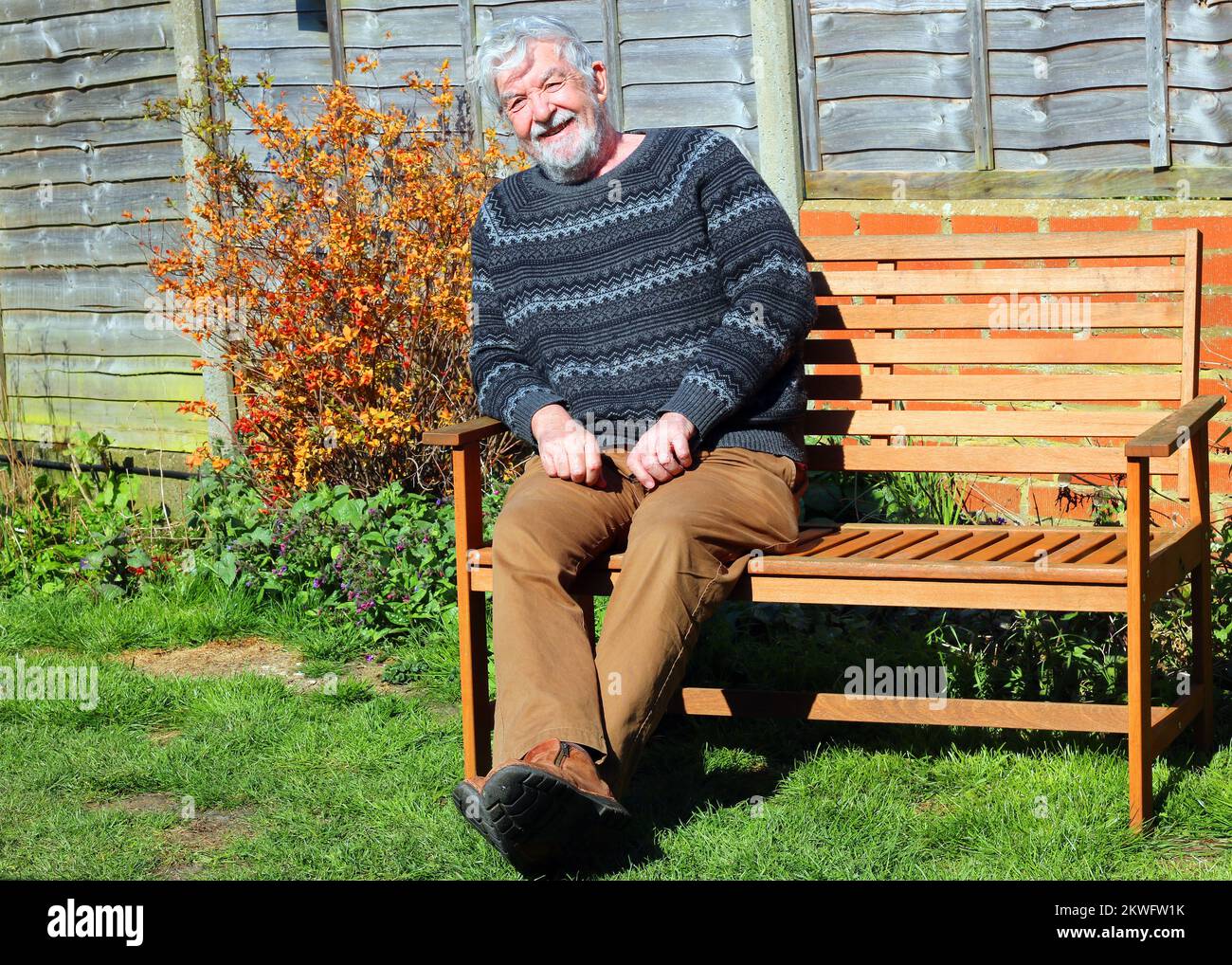 Älterer oder älterer Mann, der draußen auf einer Bank sitzt und in die Kamera lächelt. Stockfoto
