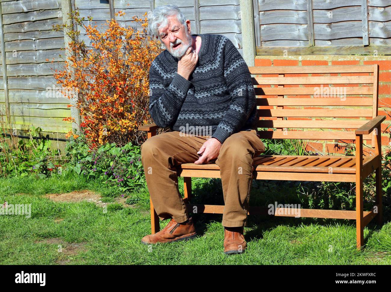 Senioren oder Senioren, die auf einer Bank sitzen. Nacken wegen Schmerzen halten. Möglicherweise Arthritis. Stockfoto