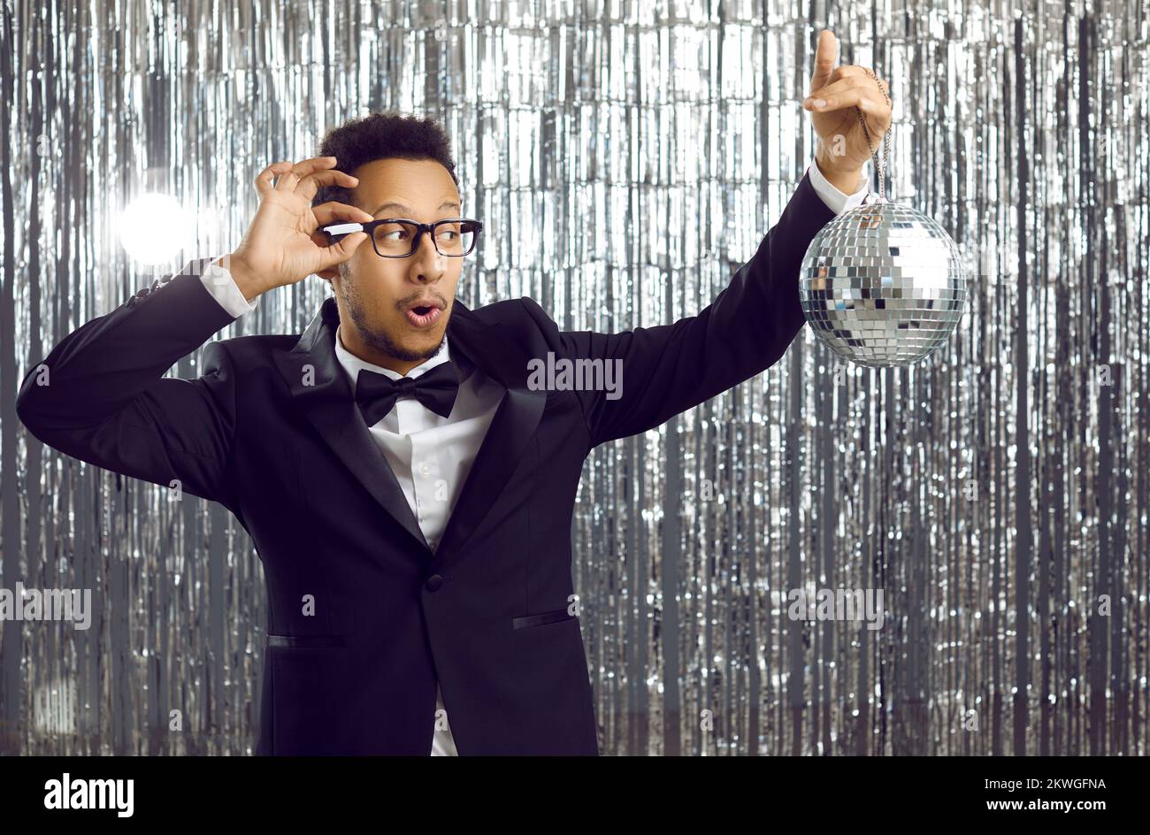 Ein glücklicher, alberner Schwarzer im Anzug, der Spaß mit einer glänzenden Spiegelkugel auf einer Disco-Party hat Stockfoto